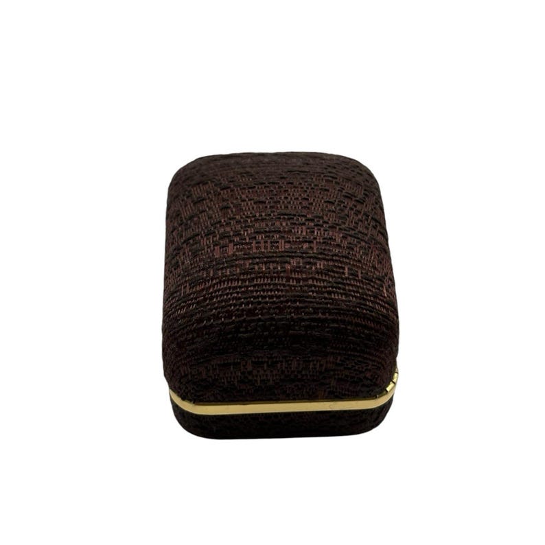 May include: A brown fabric ring box with a gold trim.