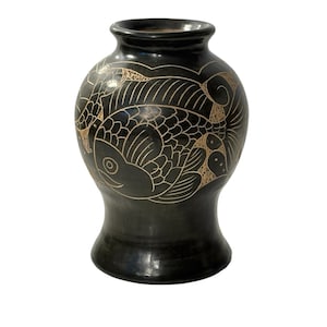 May include: A black ceramic vase with a wide base and a narrow neck. The vase features an etched design of fish and waves in a light brown color. The vase is approximately 8 inches tall.