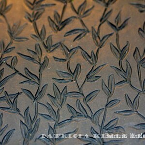 May include: A close-up of a dark brown rectangular block with a repeating pattern of carved leaves. The block is a printing stamp for creating a leaf design.