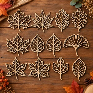 Peut inclure: Un ensemble de douze formes de feuilles en bois découpées au laser, disposées sur trois rangées. Le lot comprend diverses silhouettes botaniques comme des feuilles d'érable, de chêne et de ginkgo, avec des motifs de nervures ajourés en bois clair.