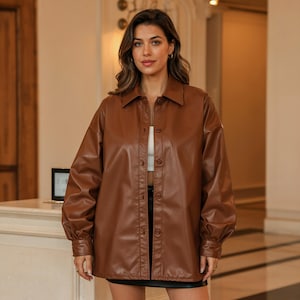 以下が含まれることがあります： ボタン留めのフロントと襟が付いた茶色のレザージャケット。 ジャケットは長袖でゆったりとしたフィット感です。 モデルは下に白いトップスを着ています。 ジャケットはミディアムブラウン色です。