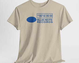 Könnte beinhalten: Beiges T-Shirt mit blauem Text "THE FINEST JAZZ SINCE 1939" in einem Rechteck und einem blauen Oval. Darunter sind die Worte "BLUE NOTE RECORDS" in Blau gedruckt.