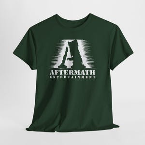 May include: Dark green t-shirt featuring a white graphic of the letter "A" with a silhouette design and the text "AFTERMATH ENTERTAINMENT" below. The shirt is made of a soft material and has short sleeves.