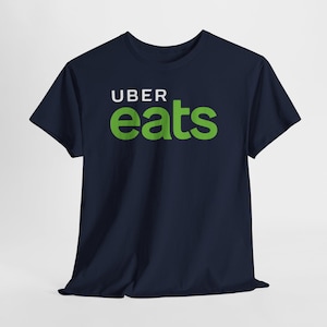 Peut inclure: T-shirt bleu marine avec le texte blanc "UBER" au-dessus du texte vert "eats". Le t-shirt est fait d'une matière douce et a des manches courtes. Le motif est centré sur le devant du t-shirt.