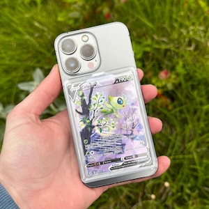Könnte beinhalten: Ein silbernes Smartphone mit einem Dreifach-Kamerasystem und einer transparenten Schutzhülle, in der eine Celebi V-Sammelkarte steckt. Die Karte zeigt ein grünes Wesen, den Text Celebi V, 190 KP sowie den Text Blattchenreigen und Rückschnitt.
