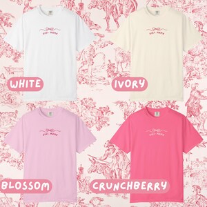 May include: Four short-sleeved t-shirts in white, ivory, blossom pink, and crunchberry pink. Each shirt has a small bow and the words "Girl Mama" printed in a cursive font. The background is a pink and white toile pattern.