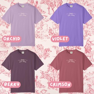 May include: Four short-sleeved t-shirts in orchid, violet, berry, and crimson. Each shirt has the text "Girl Mama" with a bow design. The shirts are displayed on a pink and white toile background.