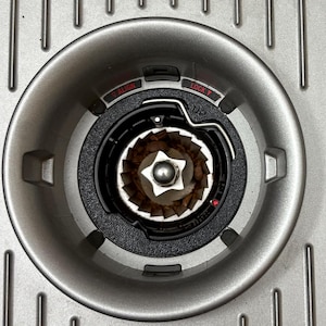 Könnte beinhalten: Nahaufnahme einer silbernen Kaffeemühle mit schwarzem und silbernem Innenraum. Die Mühle hat ein Zifferblatt mit den Wörtern "ALIGN" und "LOCK". Der Innenraum zeigt den Mahlmechanismus und Kaffeesatz.