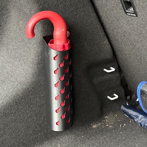 Könnte beinhalten: Ein schwarzer Regenschirmhalter mit roter Innenausstattung und einem Muster aus roten Tränen. Der Regenschirmgriff ist rot. Der Halter ist im Kofferraum eines Autos montiert. Ein teilweise sichtbarer blauer und silberner Regenschirm ist ebenfalls vorhanden.