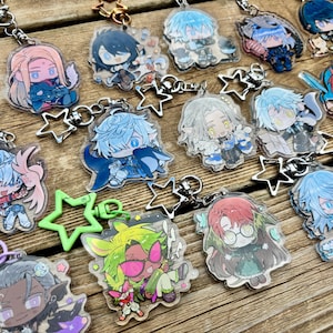 Può includere: Una collezione di portachiavi in acrilico trasparente con varie illustrazioni di personaggi in stile anime. Ogni ciondolo è fissato a una chiusura in metallo a forma di stella in colori tra cui argento, verde e viola, raffiguranti diverse figure.