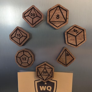 May include: A set of wooden dice magnets with numbers 4, 6, 8, 10, 12, and 20. The magnets are attached to a brown surface with a brown paper note that says "The Woodwright's Quest" and a logo with the letters "WQ" and stars.