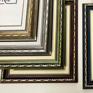 Può includere: Una collezione di cornici rettangolari con bordi decorati e in rilievo in vari colori, tra cui oro, argento, blu, verde e rosso scuro. Ogni cornice include un passe-partout color crema e un inserto bianco con il testo "INWOOD UTIQE".