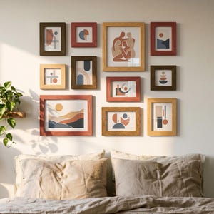 May include: A bedroom scene with a collection of framed abstract art in various sizes and colours, mounted on a white wall. A bed with neutral-toned bedding is in the foreground, with a wooden nightstand, lamp, and plants adding to the decor.