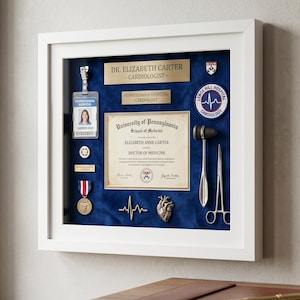 Puede incluir: Un marco de vitrina blanco que contiene un diploma médico de la Universidad de Pensilvania para Elizabeth Anne Carter, una tarjeta de identificación hospitalaria, dos placas doradas, un parche de Lenox Hill Hospital, martillo, tijeras y medalla.