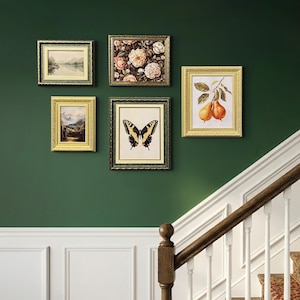 Peut inclure: Plusieurs œuvres d'art encadrées sont accrochées sur un mur vert foncé. L'art comprend des peintures de paysages, des compositions florales et une illustration de papillon. Un escalier en bois avec des balustres blancs et une moquette à motifs est en arrière-plan.