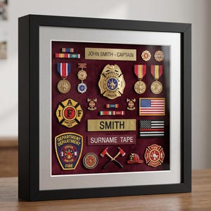 Puede incluir: Un marco de vitrina negro que contiene una colección de recuerdos de bomberos sobre un fondo de terciopelo rojo oscuro. Los artículos incluyen una insignia de bombero estadounidense, medallas, parches, pines y cintas con nombres.