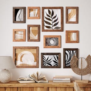 May include: A gallery wall of framed art prints featuring abstract and botanical designs. The wooden frames vary in size and shade of brown. The artwork is displayed on a white wall above a wooden cabinet, creating a stylish display.