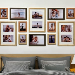Op de afbeelding: Een verzameling ingelijste foto's in verschillende formaten en oriëntaties, gemonteerd op een witte muur. De frames zijn in tinten bruin en natuurlijk hout, met familiefoto's. De opstelling omvat zowel enkele als dubbele fotolijsten.