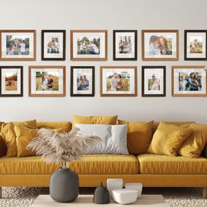 Può includere: Una composizione a parete di foto di famiglia incorniciate in vari formati e orientamenti. Le cornici sono marroni e nere, disposte sopra un divano giallo con cuscini abbinati. Un vaso grigio con piante secche decorative è su un tavolino.