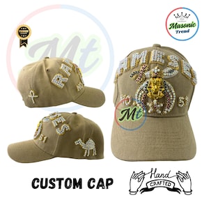 May include: A tan baseball cap with a custom design featuring rhinestones, gold accents, and the words "RIMES" and "MASONIC TREND". The cap is hand-crafted and has a curved brim.