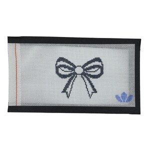 Può includere: Una tela per punto croce con un disegno a fiocco blu navy su sfondo bianco. Ha un bordo nero e un piccolo motivo floreale blu nell'angolo in basso a destra. Una striscia verticale rossa sul lato sinistro.