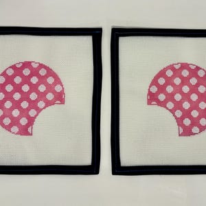 May include: Two square needlepoint canvases with a white background and a black border. Each canvas features a pink half-circle design with white polka dots. The design has a bite taken out of it.