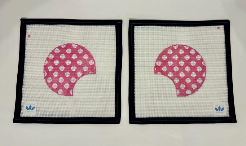 May include: Two square needlepoint canvases with a white background and a black border. Each canvas features a pink half-circle design with white polka dots. The design has a bite taken out of it.