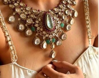 May include: A gold necklace with a large, teardrop-shaped blue gemstone surrounded by smaller diamonds and emeralds. The necklace has a delicate, intricate design and is adorned with numerous smaller gemstones.