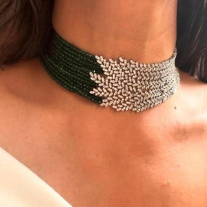 Puede incluir: Un collar choker de varias capas con cuentas verdes y un gran diseño brillante en forma de diamante en el centro.