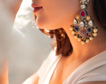 May include: A pair of large, ornate earrings with a gold base and a variety of colorful gemstones, including red, blue, and green. The earrings are decorated with pearls and have a teardrop shape.
