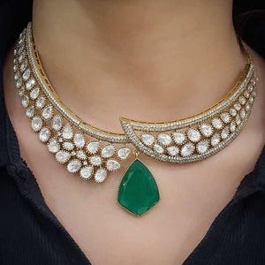 Op de afbeelding: Een gouden ketting met een grote groene edelsteen hanger en een delicaat ontwerp van kleine witte stenen.