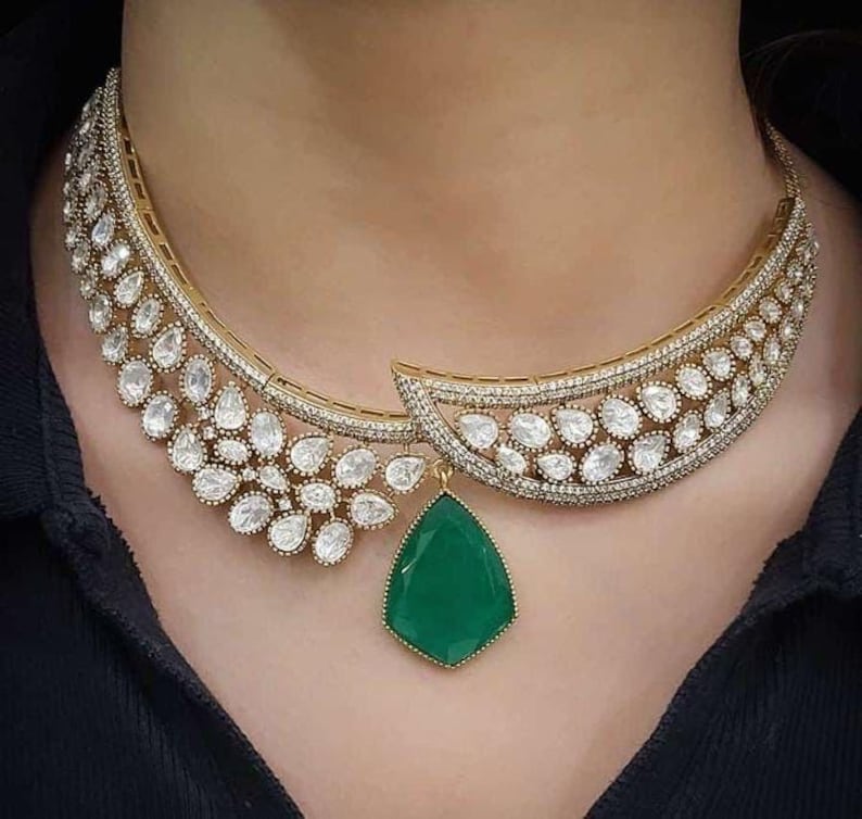 Op de afbeelding: Een gouden ketting met een grote groene edelsteen hanger en een delicaat ontwerp van kleine witte stenen.