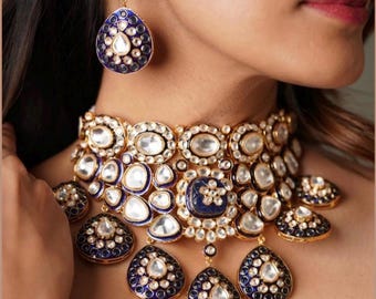 May include: A gold and blue statement necklace with a choker style and multiple teardrop pendants. The necklace is adorned with white stones and blue enamel.