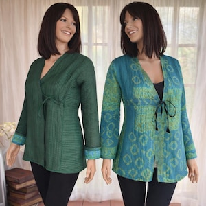 Puede incluir: Dos maniquíes con chaquetas de manga larga y pantalones negros. Una chaqueta es verde liso, la otra es turquesa con un estampado verde. Ambas chaquetas tienen un lazo en la cintura y se combinan con bailarinas negras.