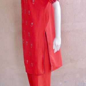 Könnte beinhalten: Ein rotes, besticktes Salwar Kameez mit schwarzen und weißen Blumenmustern. Das Outfit besteht aus einer langen Tunika mit seitlichem Schlitz und einer passenden Hose.