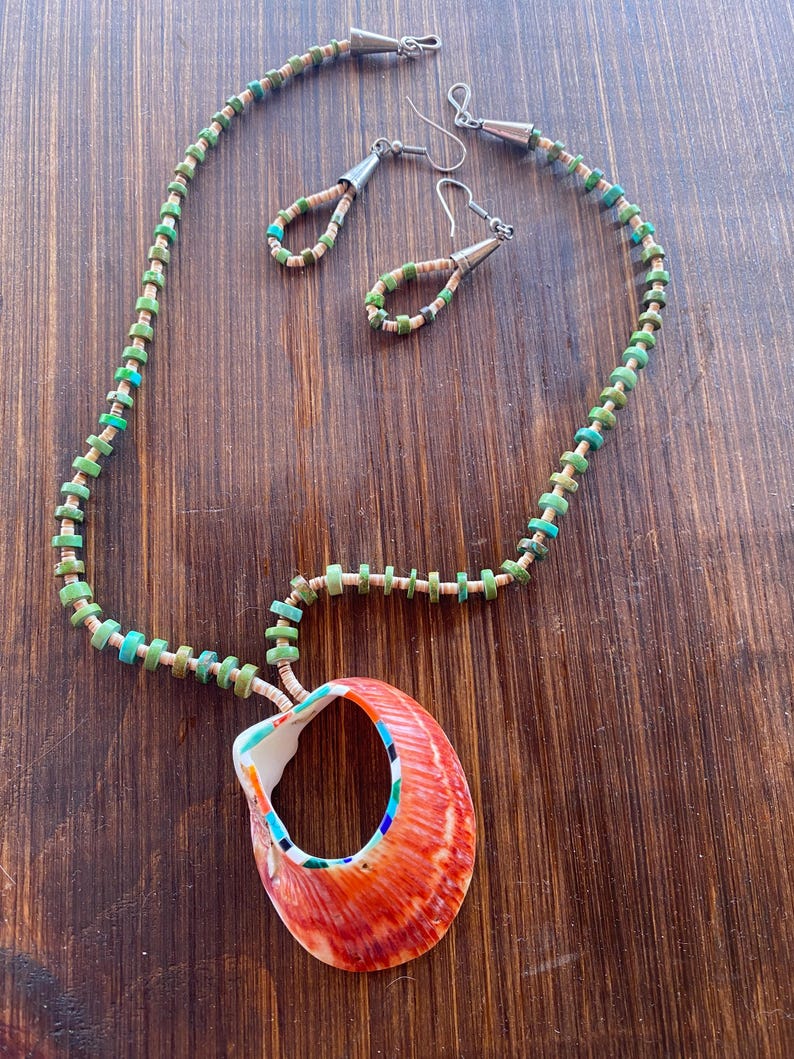 May include: A handmade necklace and earring set featuring a large, orange seashell pendant. The necklace and earrings have turquoise and green beads. The seashell pendant has a colorful interior.