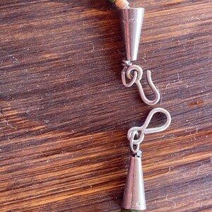May include: A close-up of a necklace with a silver clasp. The necklace features small, square, turquoise and green beads interspersed with off-white shell beads. The clasp is a simple hook and eye design.