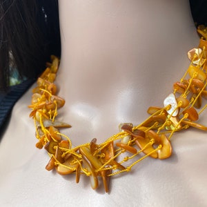 Peut inclure: Un collier multi-rangs composé de coquillages de couleur brun doré de forme irrégulière enfilés sur un fil jaune.
