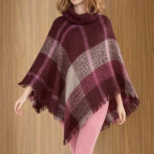 Könnte beinhalten: Ein bordeauxfarbener Poncho mit Karomuster, Rollkragen und Fransen. Der Poncho hat ein Muster aus bordeauxfarbenen, rosa und grauen Quadraten. Das Model trägt eine rosa Hose.
