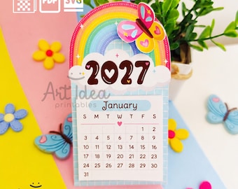 Peut inclure: Un calendrier imprimable de janvier 2027 avec un arc-en-ciel, un papillon coloré et une grille. Le design inclut le texte 2027, January et Art Idea printables. Des icônes pour les formats PNG, PDF et SVG sont affichées en haut.