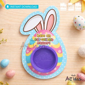 Puede incluir: Un soporte de Play-Doh con temática de Pascua con forma de conejito con el texto "have an egg-cellent easter!". El soporte es azul con lunares blancos y un recipiente de Play-Doh morado. Huevos de Pascua están esparcidos alrededor del soporte.