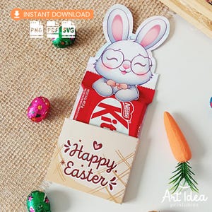 Può includere: Una confezione regalo pasquale con una barretta Kit Kat, decorata con un coniglietto dei cartoni animati con gli occhiali. La scatola color crema ha il testo "Buona Pasqua" e un motivo a quadri. Include una carota e uova di cioccolato confezionate.