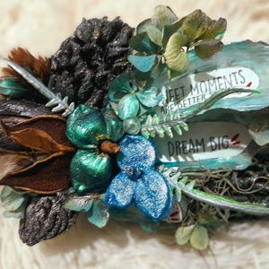 Könnte beinhalten: Ein Mixed-Media-Kunstwerk mit getrockneten Blumen, Samenkapseln und dekorativen Elementen in Türkis, Braun und Silber. Der Text "SWEET MOMENTS ARE BETTER" und "DREAM BIG" ist sichtbar.