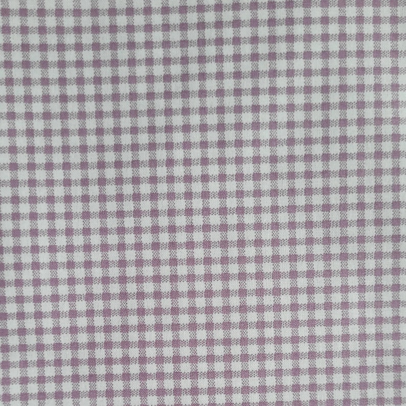 Pode incluir: Close-up de um tecido com padr&atilde;o xadrez vichy. O tecido apresenta um padr&atilde;o quadrado repetitivo em um esquema de cores roxo claro e branco. O padr&atilde;o &eacute; uniformemente espa&ccedil;ado e cria um visual cl&aacute;ssico e texturizado, adequado para v&aacute;rios projetos de artesanato.
