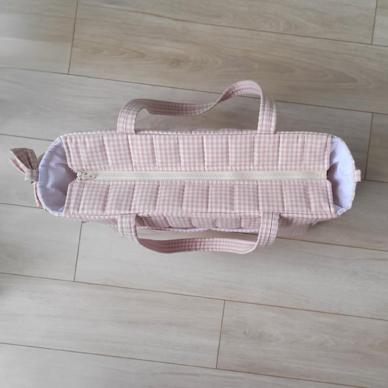 Pode incluir: Uma bolsa tote rosa e branca com padr&atilde;o xadrez, com fecho de correr e duas al&ccedil;as. A bolsa tem um design acolchoado e um detalhe de la&ccedil;o de um lado. O interior &eacute; branco.