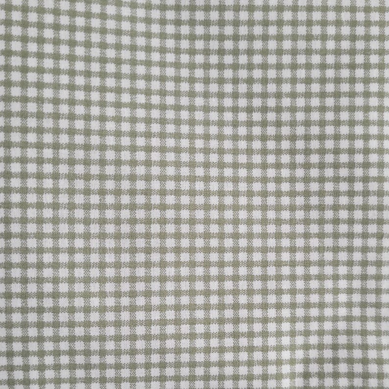 Pode incluir: Close-up de um tecido com padr&atilde;o xadrez. O padr&atilde;o apresenta uma grade de quadrados pequenos e uniformemente espa&ccedil;ados em cor verde claro sobre um fundo branco. O tecido tem uma apar&ecirc;ncia ligeiramente texturizada.