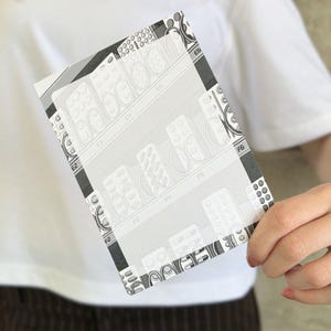 Könnte beinhalten: Eine rechteckige Karte mit einem schwarz-weißen Gittermuster aus Tablettenblistern. Das Design zeigt wiederkehrende Reihen von Medikamentenverpackungen mit kreisförmigen Vertiefungen und klaren Beschriftungen wie E3, E4, E5, F3, F4, F5 und F6.