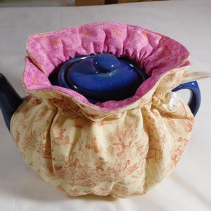 May include: A blue teapot with a cream and red floral patterned tea cozy. The cozy has a pink lining and a white drawstring.