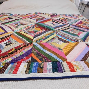 May include: A colorful patchwork quilt with a diamond pattern. The quilt is made from a variety of fabrics in different colors and patterns. The quilt is on a white bed.