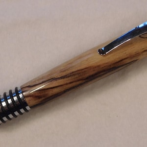 Il s'agit d'un stylo clic spartiate tourné à la main avec un corps en orme écaillé qui a un look industriel. Ses dix joints toriques complètent le look 523